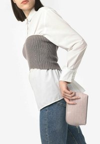 Szary, dzianinowy, krótki top nałożony na białą koszulę, w zestawieniu z niebieskimi dżinsami. Trzyma różową torebkę koktajlową z wytłoczeniem w kształcie krokodyla.