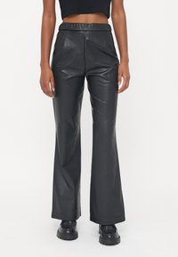 Zwarte leren broek met een gladde textuur, hoge taille en wijdvallende pijpen. Kenmerken zijn onder andere zijzakken en een subtiele glans.