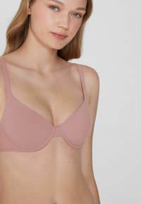Gevormde bh met een lichte roze stof, met een gladde textuur en verstelbare bandjes. Kenmerkt zich door een naadloos ontwerp en beugels voor ondersteuning.