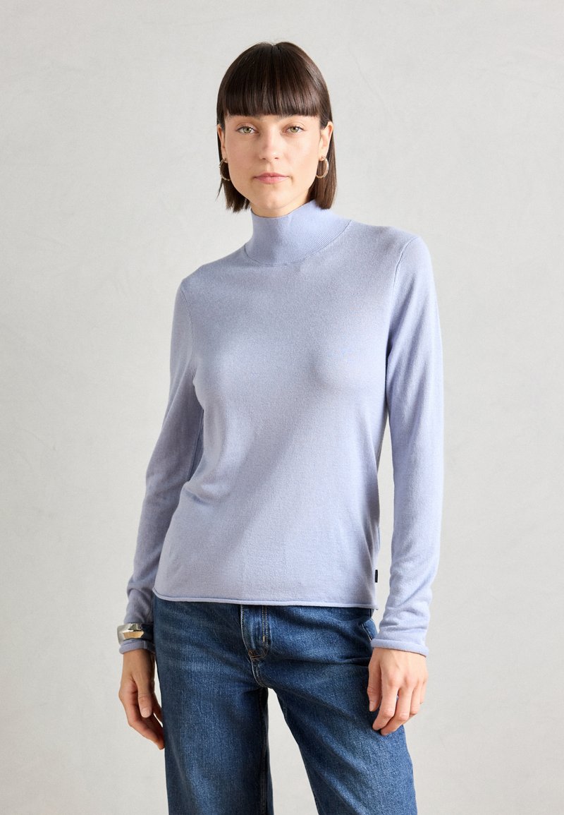 Light purple long-sleeve turtleneck sweater in soft fabric, featuring a fitted silhouette and ribbed neckline. Paired with blue jeans.