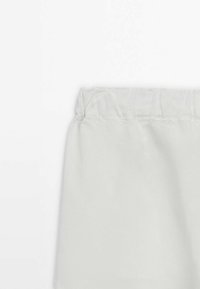 Lichtgrijze stoffen broek met een elastische tailleband en een soepele textuur. De stof lijkt enigszins gekreukt met een matte afwerking.