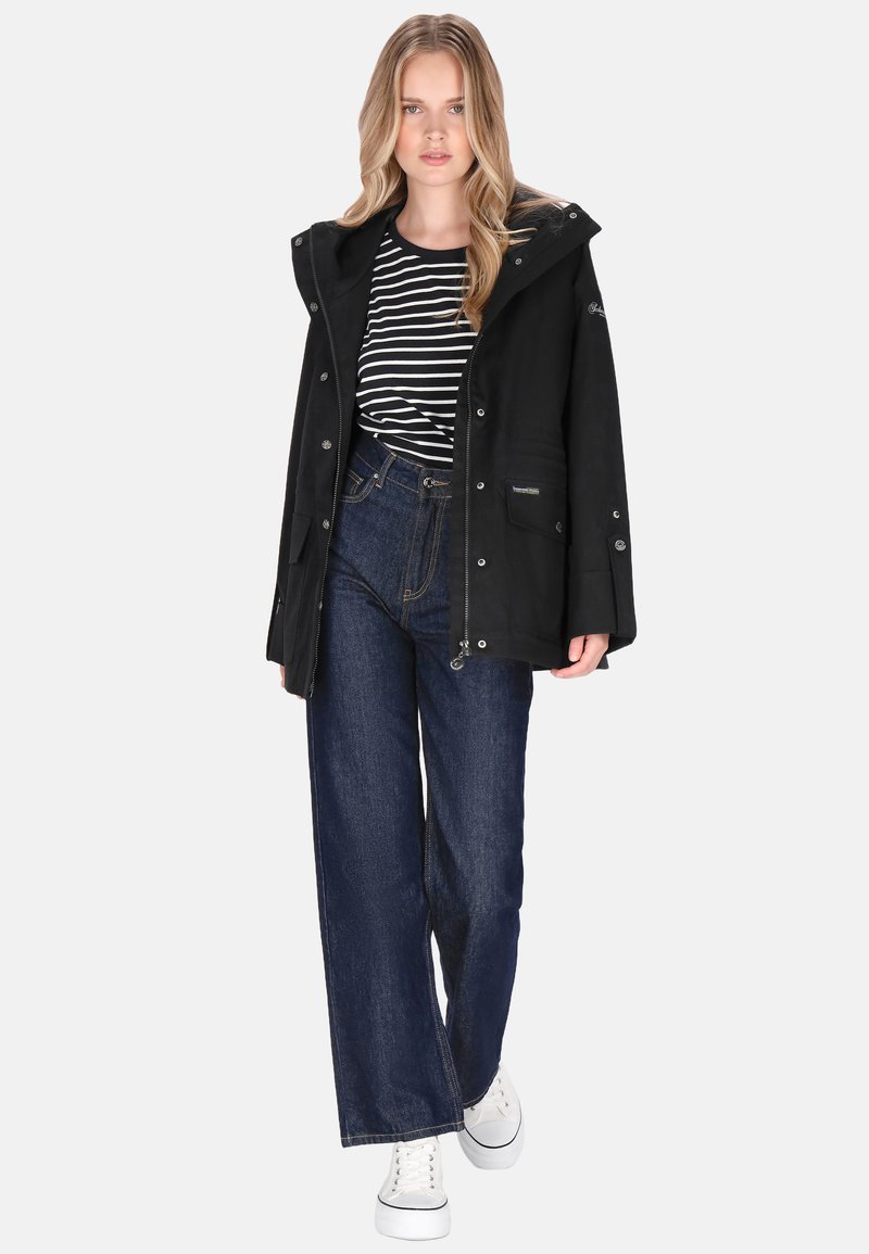 Fekete vízálló dzseki kapucnival, csíkos inggel, magas derekú kék farmerrel és fehér tornacipővel párosítva.