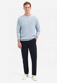 Lichtblauwe geribbelde trui met een ronde halslijn, gecombineerd met marineblauwe broek en witte sneakers, wat een casual outfit creëert.