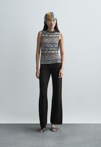 Αμάνικο μπλουζάκι με ζικ-ζακ σχέδιο σε μαύρο, λευκό και πορτοκαλί χρώμα, συνδυασμένο με εφαρμοστά μαύρα παντελόνια που ανοίγουν από το γόνατο. Το μοντέλο φοράει ένα καρώ κορδέλα στο κεφάλι.