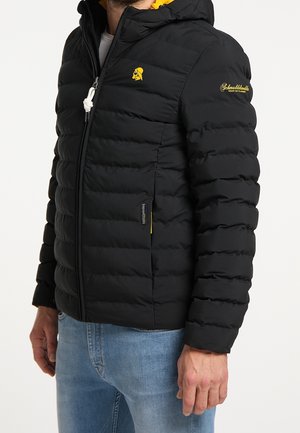 Chaqueta acolchada negra con forro amarillo en la capucha, cremallera frontal, logotipo en el pecho y bolsillos laterales. Presenta una textura acolchada y puños elásticos.