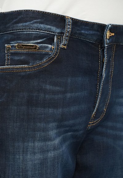 Sötétkék farmernadrág narancssárga varrásokkal, fémből készült gombbal és apró elülső zsebbel, amelyen fekete és arany "Dsquared2" márkacímke található.