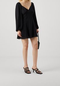 Svart miniklänning med puffärmar, V-ringning och flödande tyg. Matchad med svarta sandaletter med remmar och en liten svart handväska.