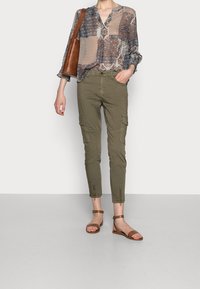 Lightweight printed blouse with three-quarter sleeves, paired with olive green cargo pants featuring zippered ankles, and brown flat sandals.