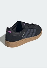 Sneaker in suede nero con suola in gomma, caratterizzata da strisce grigie pixelate, accenti viola e suola esterna in gomma testurizzata color crema. Logo sul lato.