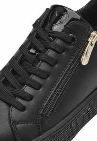 Sneaker in pelle nera con suola texturizzata, design con lacci, dettagli lucidi neri e zip laterale. Include accessori in oro.