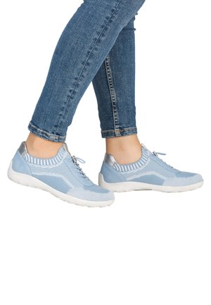 Persoon met lichtblauwe gebreide sneakers met witte zolen en metalen hielaccenten, gecombineerd met blauwe opgerolde skinny jeans.