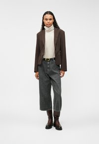 Brūns piegrieztā žakete pār beigu krāsas turtlenecku, apvienota ar augsto jostasvietu pelēkiem džinsu culotte un līdz ceļgaliem burgundu krāsas zābakiem.