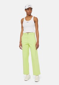 Valkoinen toppi, jossa on "DICKIES"-logo, kirkkaan vihreät leveälahkeiset housut, valkoiset sneakerit ja valkoinen lippalakki mustalla logo-yksityiskohdalla.