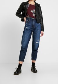 Černá kožená motocyklová bunda přes květinovou blůzu; opotřebované modré džíny s ohrnutými lemy; černé boty s tkaničkami.