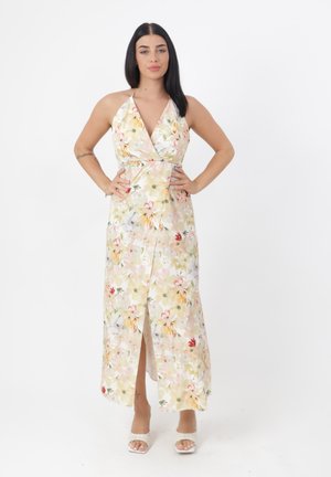 Mujer con vestido sin mangas de flores y cuello halter con una abertura frontal, de pie con las manos en las caderas sobre un fondo blanco liso.