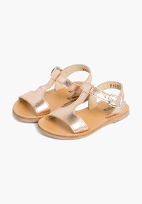 Sandali metallici color oro rosa con due cinturini, una fibbia e un design a intaglio. Leggeri, con una suola testurizzata e una finitura liscia.
