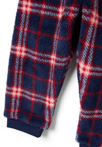 Tejido de felpa suave con un patrón a cuadros en rojo, blanco y azul, y puño de canalé azul marino en una prenda de manga larga.