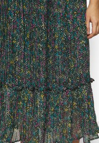 Musta kukkamekko, jossa on pleatattu muotoilu ja monivärisiä kukkia vaaleanpunaisena, keltaisena ja sinisenä. Sateen alta löytyvä röyhelö helmassa tuo lisäyksityiskohtia.