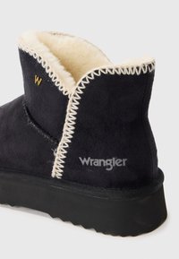 Fekete nubuk bokacsizma krém színű műszőrme bélésse, kontrasztos fehér varrással, Wrangler ezüst logóval és texturált fekete gumitalppal.