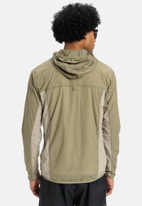 Letajkt i khaki med hætte og kontrasterende beige sidepaneler. Struktureret stof, lange ærmer og en tætsiddende silhuet.