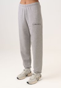Šedé tepláky s elastickým pásom, manžetami na členkoch a čiernym nápisom "LAMANIA" na ľavom stehne. Mäkký materiál a voľný strih.