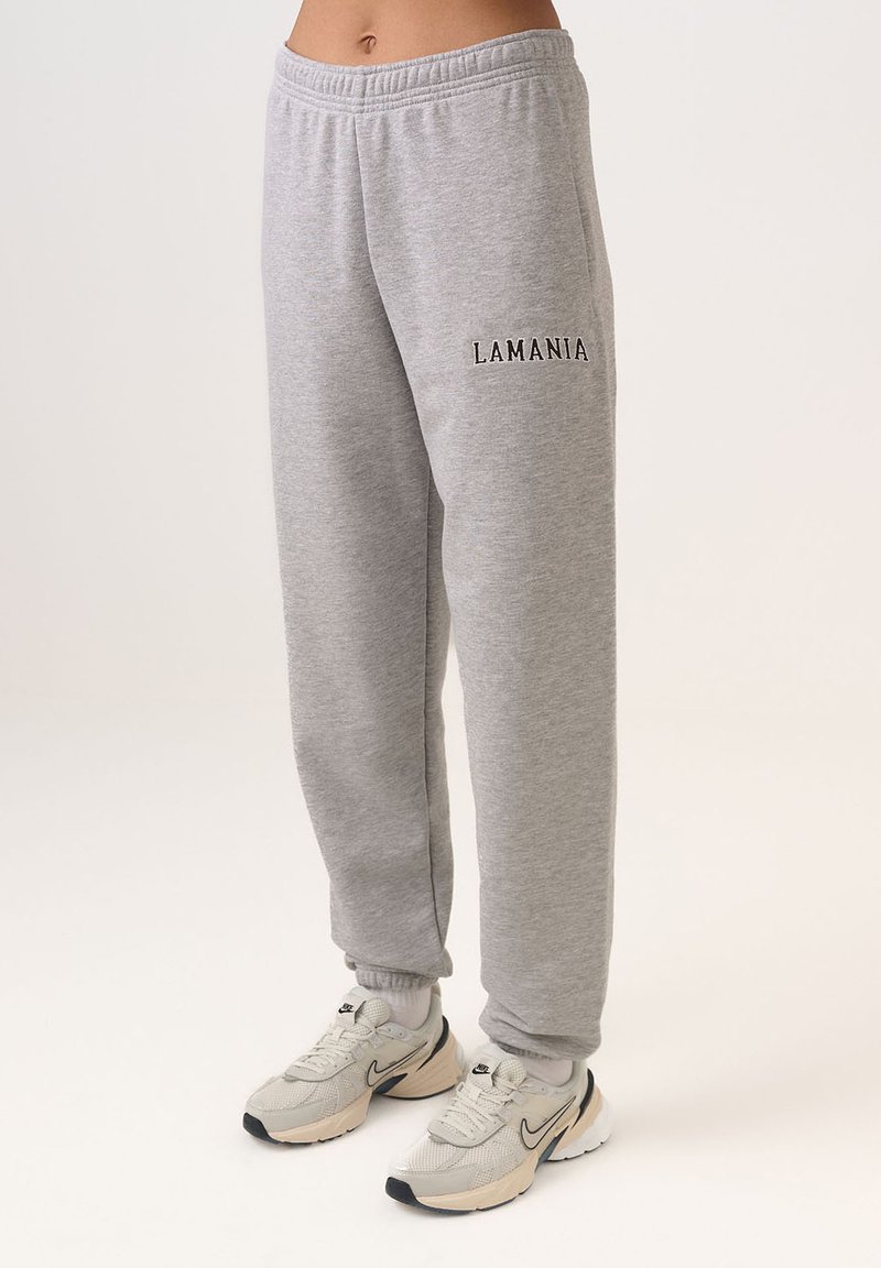 Šedé tepláky s elastickým pásom, manžetami na členkoch a čiernym nápisom "LAMANIA" na ľavom stehne. Mäkký materiál a voľný strih.