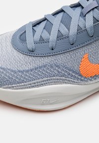 Lysblå sneakers med en struktureret strikoverdel, kontrasterende orange logo og en hvid polstret sål. Snørebåndene er blå med en glat finish.