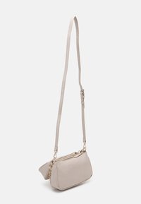 Béžová crossbody taška vyrobená z texturovaného materiálu, s dlouhým nastavitelným popruhem a dvojitými zipovými přihrádkami. Akcenty ve zlatém tónu.