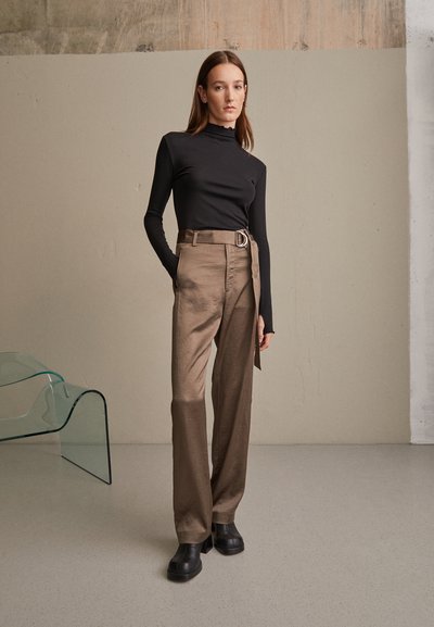 Top negro de manga larga combinado con pantalones de tiro alto beige que cuentan con un cinturón en forma de D y zapatos de plataforma negros. Texturas suaves y diseño moderno.