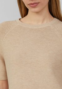 Beige gestrickter Pullover mit kurzen Ärmeln und einem runden Ausschnitt, der eine glatte Textur und dezente Rippdetails am Kragen aufweist.