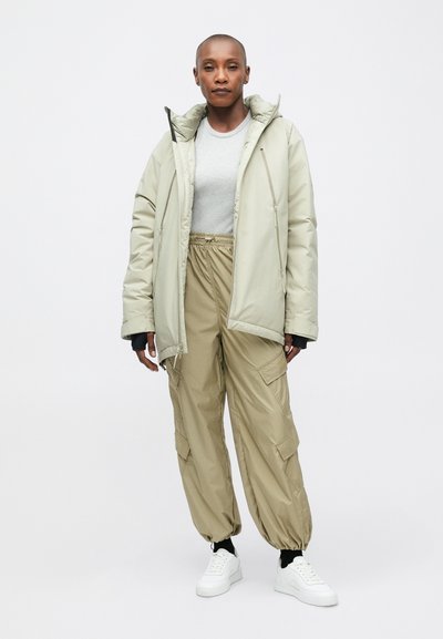 Beige pufi dzseki kapucnival, laza illeszkedésű cargo nadrággal párosítva. Fehér sportcipő. Puha tapintás, egyszerű dizájn és semleges színpaletta.