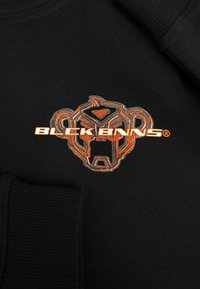 Zwarte sweatshirt met een opvallend oranje en zilver geborduurd logo van een gestileerd aap gezicht met de tekst "BLCK BNNS" eronder.