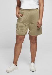 Beige bomullsshorts med elastisk midje, sidelommer og avslappet passform, kombinert med hvite sneakers og en enkel hvit topp.