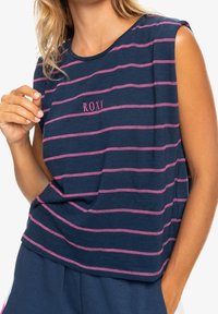 Marinblårandig ärmlös topp med rosa horisontella ränder. Har en rund halsringning och ordet "ROXY" broderat i rosa på framsidan.