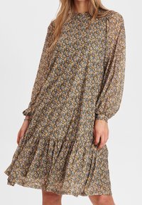 Floral dress featuring long sleeves, a high neckline, and a tiered hem. Made of lightweight fabric in a multicolored floral pattern.