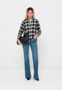 Svart-hvitt rutete skjorte med knapper, blå flagrende jeans og en svart veske. Antrekket har en avslappet passform med klassiske mønstre og teksturer.