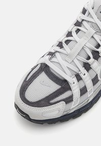 Fehér és szürke sportcipő, hálós felsőrésszel, velúr részletekkel, megerősített burkolatokkal és érdes gumitalppal a jobb tapadásért.