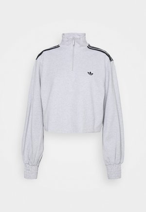 Sweat-shirt court gris clair à manches longues, col montant demi-zip, bandes noires sur les épaules et petit logo Adidas sur la poitrine.