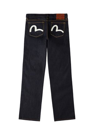 Jeans in denim blu scuro mostrati da dietro con disegni bianchi curvi su entrambe le tasche posteriori e una toppa in pelle marrone sulla cintura.