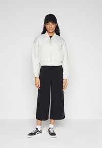 Quiltad bomberjacka i ljusgrått med ribbad nederkant, kombinerad med svarta culottes och svarta sneakers. Har dragkedja och sidfickor.