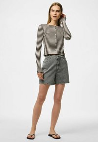 Černobílé pruhované triko s dlouhým rukávem a knoflíky, v kombinaci se šedými denimovými šortkami. Model má na sobě černé žabky. Jednoduchý, ležérní design.