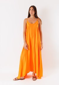 Abito maxi arancione senza maniche con una gonna fluida, realizzato in un tessuto lucido, dotato di sottili spalline e orlo leggermente curvato.
