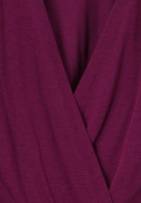 Top wrap en prune profond, avec un tissu tricoté texturé, un design en v et des détails de couture subtils le long des coutures. Matériau doux et extensible.