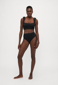 Melna mežģīņu bikini komplekts ar teksturētu, rakstainu topu, kas ir dekorēts ar volāniem un augsto vidukli. Gluda, pieguļoša silueta.