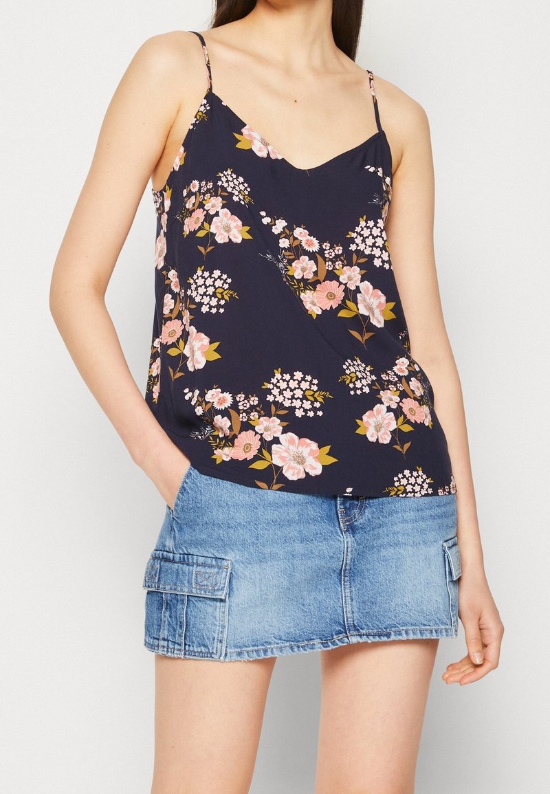 Femme portant un haut sans manches bleu marine à fleurs et une mini-jupe en jean bleu clair avec poches latérales.