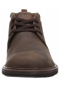 Zapato de cuero marrón con cordones, de punta redondeada y suela oscura, mostrado desde una vista cercana frontal, con detalles de costura.