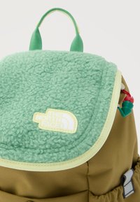 Πράσινο φλις πτερύγιο με το λογότυπο The North Face σε ταμπά σακίδιο, με πράσινες και κόκκινες κορδόνια τραβήγματος και υφασμάτινη λαβή στην κορυφή.