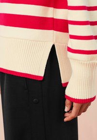 Stribet sweater i crème og pink med ribbet kant og ærmer. Har sideåbninger og tekstureret stof, parret med sorte bukser.