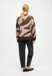 Pull en tricot marron et rose avec une texture côtelée et un motif abstrait, associé à un pantalon gris foncé et des ballerines noires.