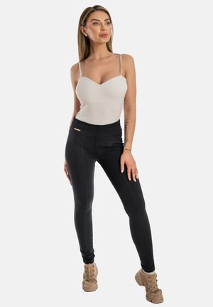 Leggings neri a vita alta con tasche con zip, abbinati a un body aderente di colore chiaro con spalline sottili. Tessuto liscio in tutto.
